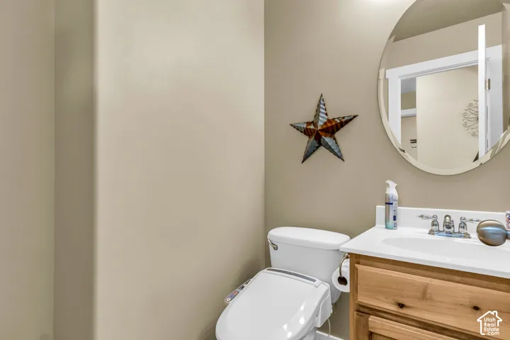 White toilet with a bidet attachment, single vanity with wood-finish cabinetry, integrated sink, and an oval mirror
