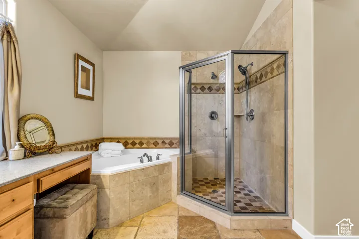 Corner soaking tub, tiled shower with glass enclosure, wood-finish cabinetry, and stone-finish floor tiles