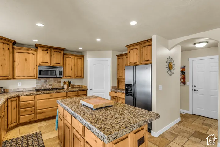 Kitchen featuring wood cabinetry, stone countertops, stainless steel appliances, recessed lighting, and tile flooring