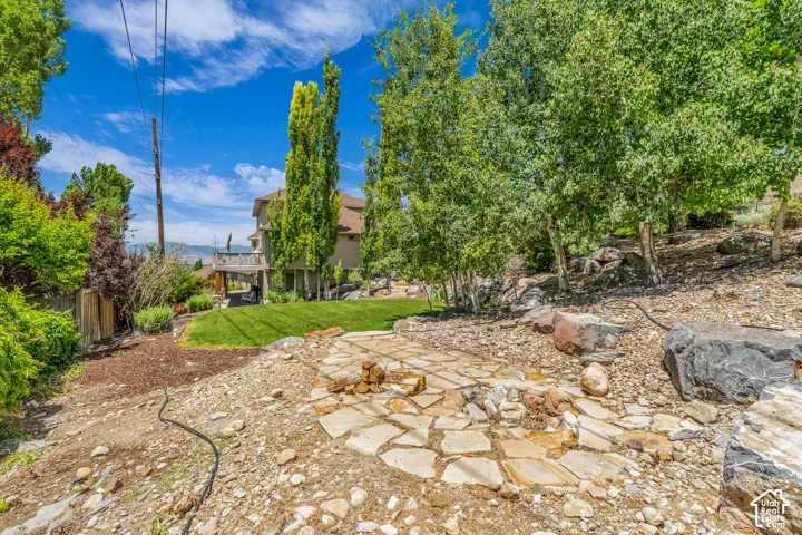 Expansive outdoor area featuring a flagstone patio, sloped landscaping, and mature trees