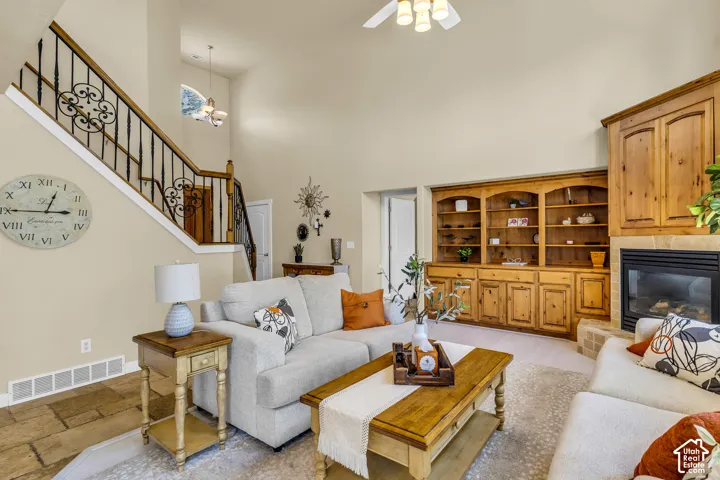 Vaulted ceiling, built-in shelving, built-in media cabinet, fireplace with stone surround, and wrought iron staircase railing