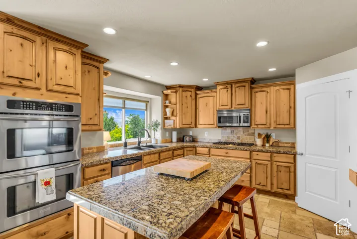 Wood-finish cabinetry, stainless steel double wall ovens, granite-style countertops, stainless steel microwave, and a tile backsplash