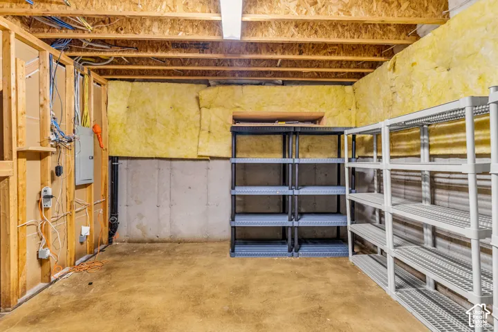 Unfinished basement space with exposed wooden joists, insulated walls, concrete flooring, and built-in shelving units