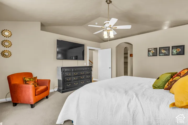 Vaulted ceiling with ceiling fan, wall-mounted television, arched doorway, and built-in shelving