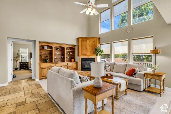 Vaulted ceiling with a ceiling fan, a fireplace with a wood surround and brick hearth, wood built-in cabinetry, an array of windows, and stone-finish flooring