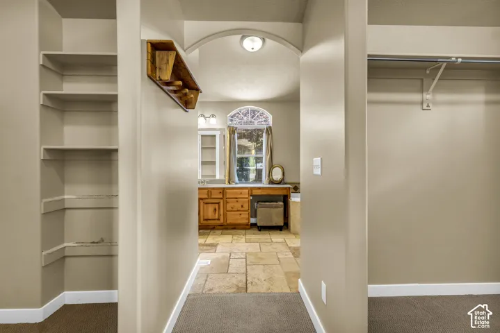 Arched hallway entrance leading to a room featuring a vanity with wood-finish cabinetry, a built-in bathtub, and a tiled floor