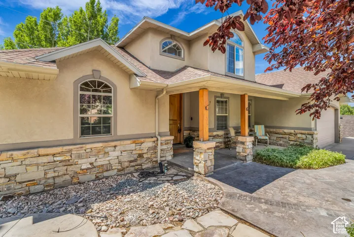 Stucco exterior with stone veneer accents, arched windows, covered porch with stone-wrapped columns and wood posts, and an attached garage