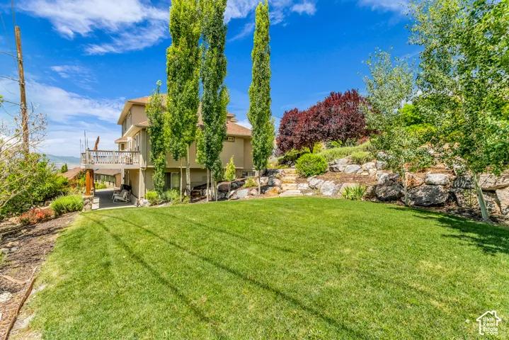 Expansive lawn area with a multi-level rock retaining wall, mature trees, and a wooden deck