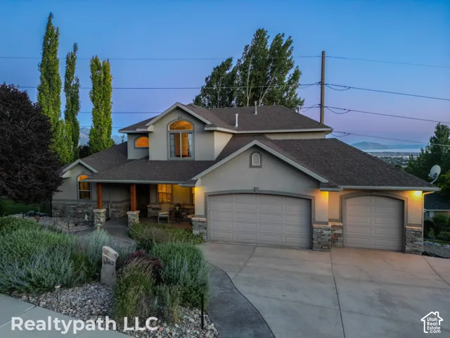 Stucco exterior with stone accents, covered front porch with wood columns, arched windows, attached double garage, and a concrete driveway
