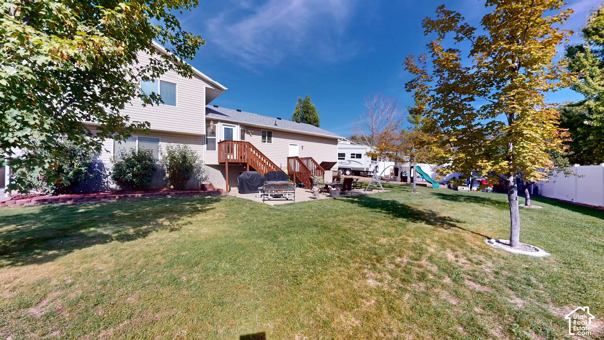 Expansive backyard featuring a manicured lawn, established trees, a concrete patio, and a privacy fence
