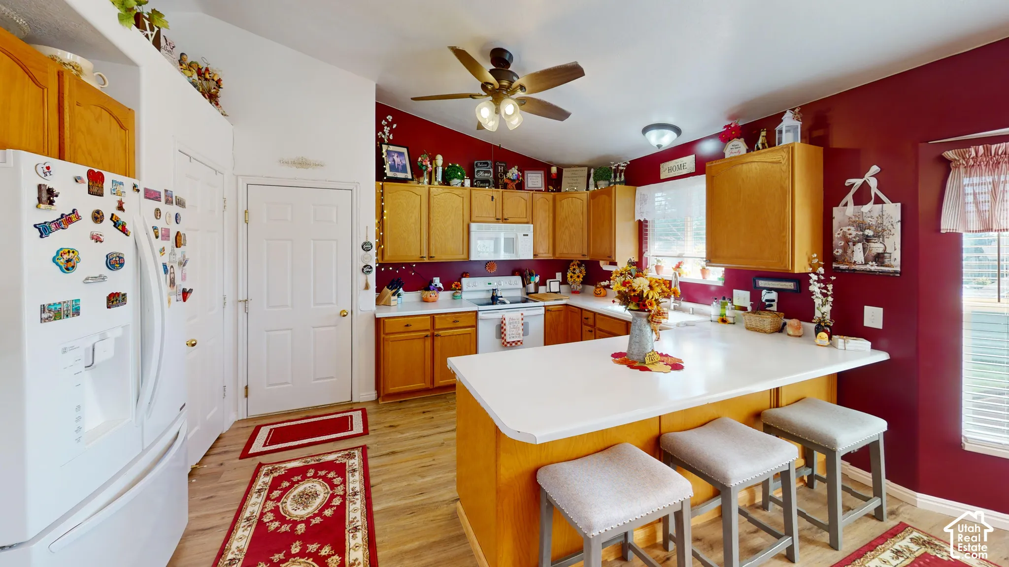 Kitchen featuring wood-finish flooring, light wood cabinetry, white appliances, and a central island with countertop seating