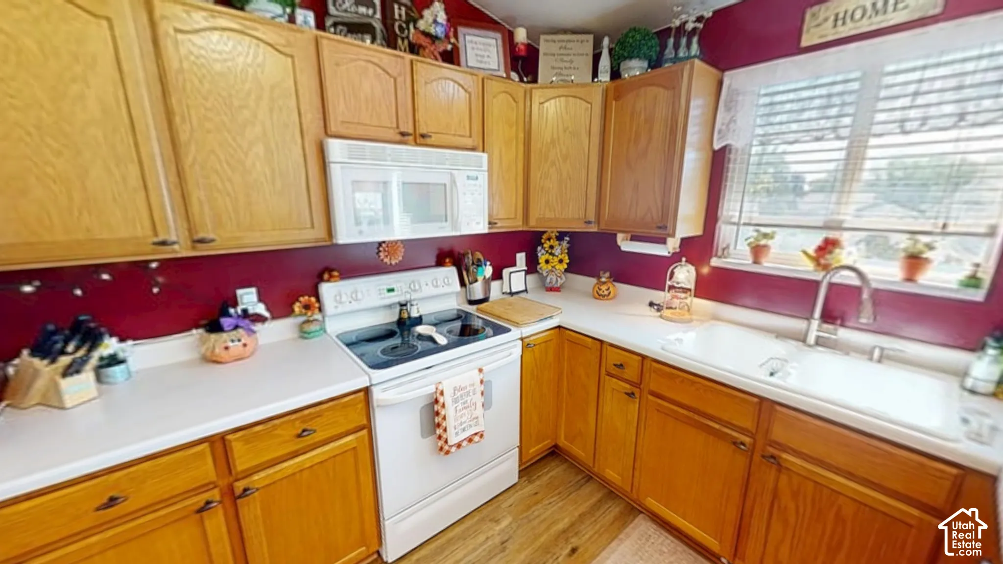 Wood-finish cabinetry, white countertops, built-in microwave, white electric range, and a single-basin sink with a gooseneck faucet