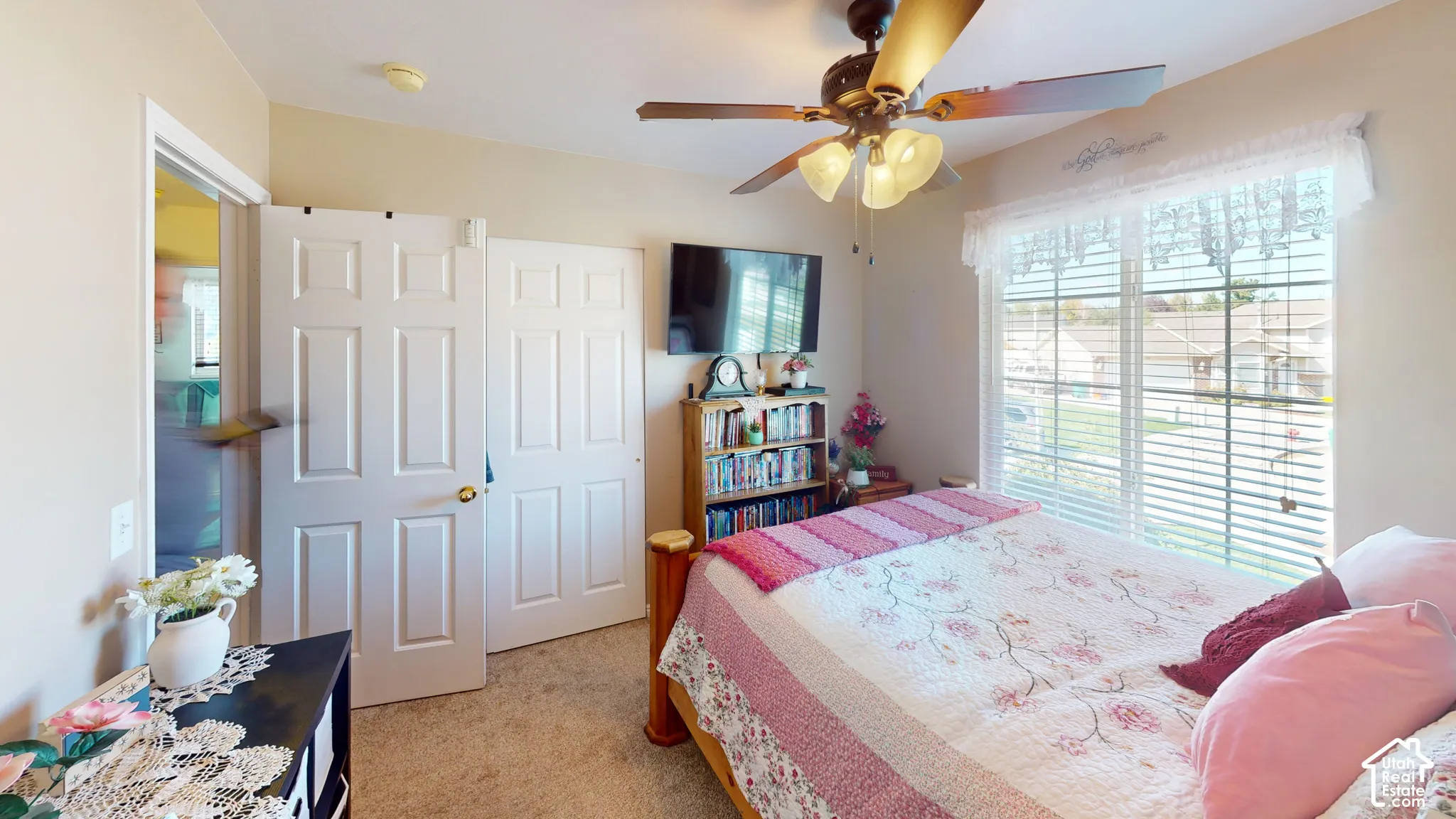 Ceiling fan light fixture, carpeted flooring, window with horizontal blinds, six-panel interior doors, and a built-in bookshelf