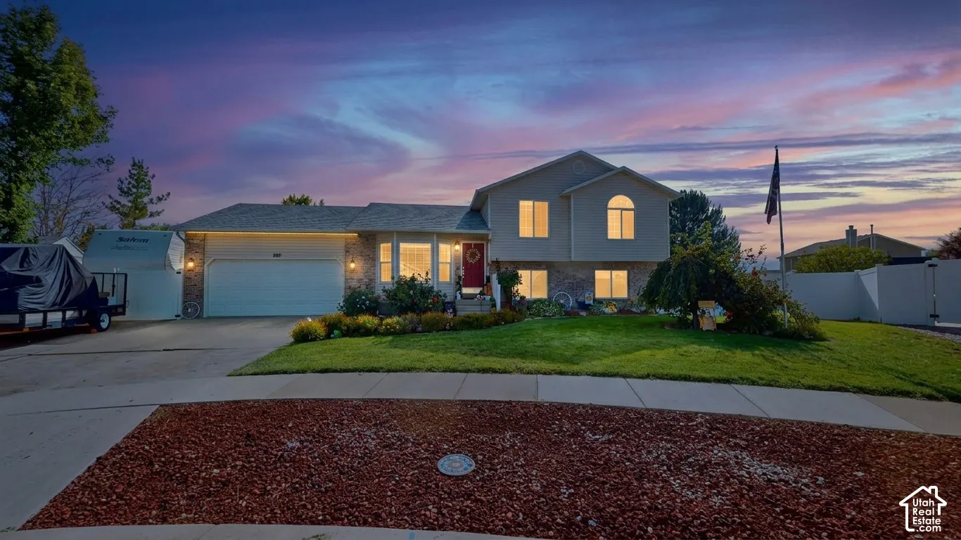 Attached two-car garage, manicured lawn, front landscaping, paved driveway, and perimeter fencing