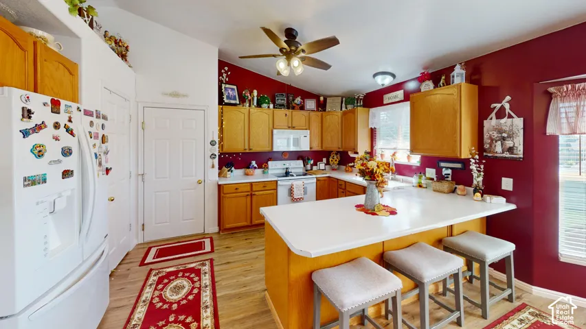 Kitchen featuring wood-finish flooring, light wood cabinetry, white appliances, and a central island with countertop seating