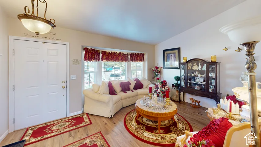Vaulted ceiling, wood-finish flooring, bay window, white walls, and an overhead decorative light fixture