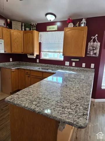 Kitchen featuring natural-finish wood cabinetry, stone-patterned countertops, an integrated undermount sink, wood-finish flooring, and a flush-mount ceiling light