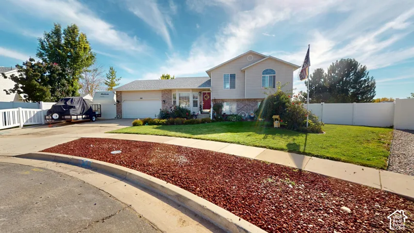 Split-level residence featuring a two-car garage, manicured front lawn, and mature landscaping