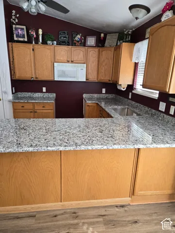 Kitchen featuring wood cabinetry, stone-surface countertops, built-in microwave, integrated dual-basin sink, and wood-finish flooring
