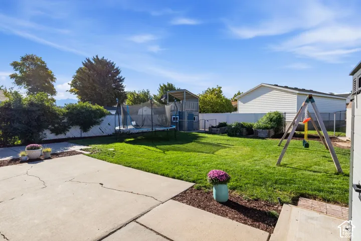 Expansive lawn with concrete patio, mature perimeter landscaping, and a chain link fence