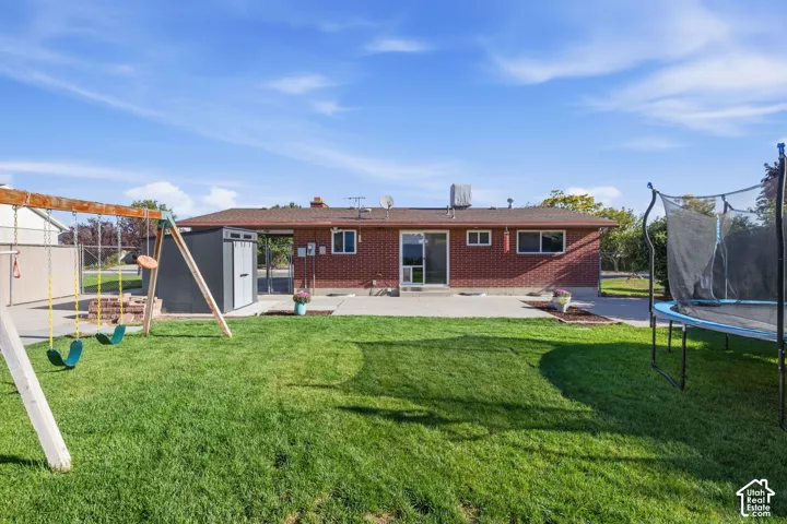 Expansive grassy backyard with a concrete patio, brick exterior, and a built-in storage shed