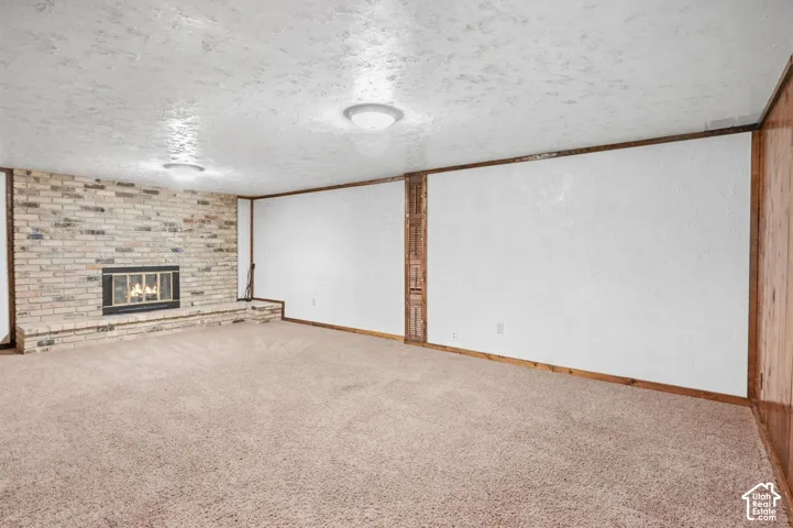 Spacious room featuring a brick-clad fireplace, light-toned carpeting, wood wall paneling, and ceiling-mounted lighting fixtures