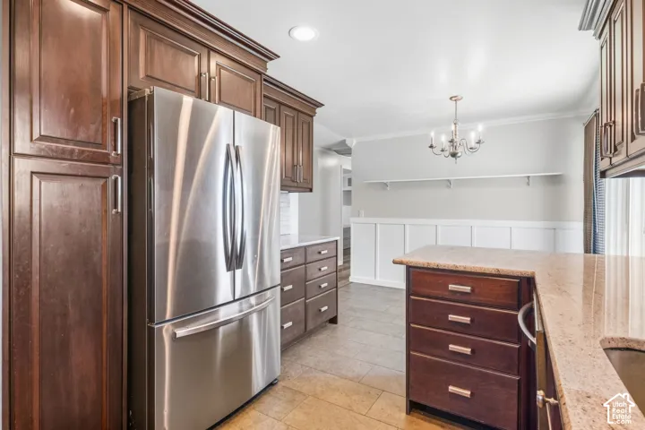 Stainless steel French door refrigerator, dark wood-finish cabinetry, light-toned countertop, tile flooring, and a chandelier lighting fixture