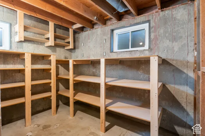 Utility space featuring wood shelving, exposed ceiling joists, and a window