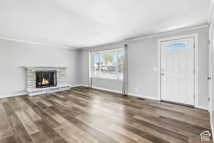 Spacious living area featuring wood-finish flooring, a stone-clad fireplace with hearth, and a window with blinds
