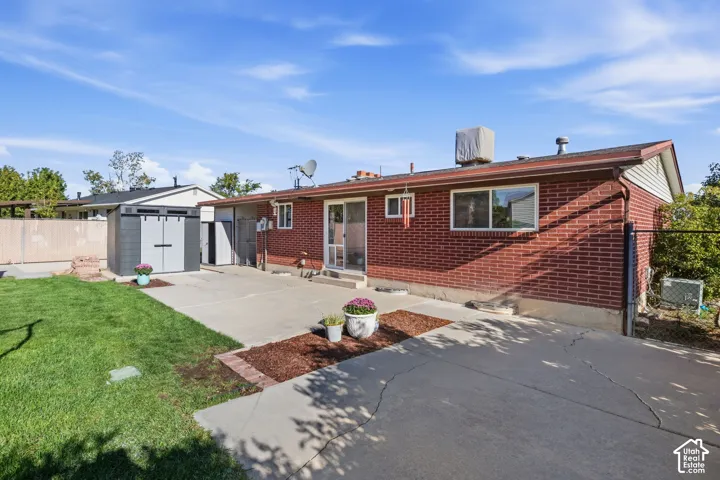 Brick exterior with a concrete patio, sliding glass door, and a storage shed