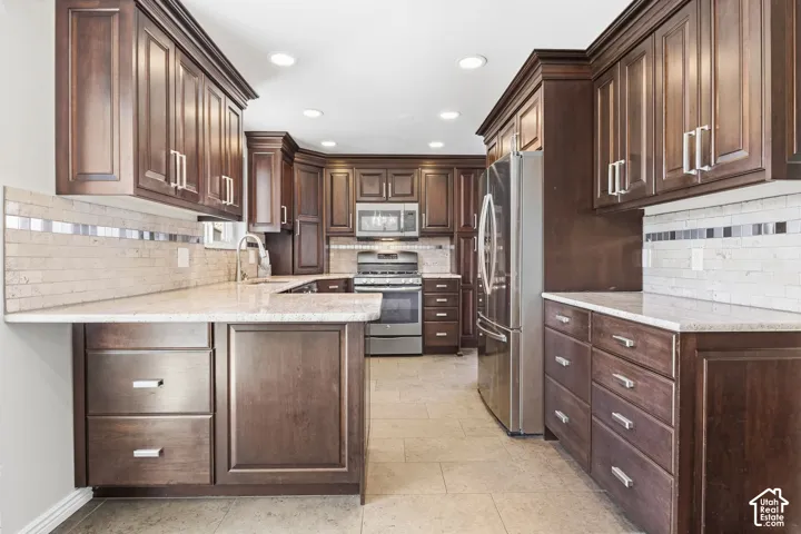 Dark wood-finish cabinetry with crown molding, granite-style countertops, stainless steel appliances, and a tiled backsplash