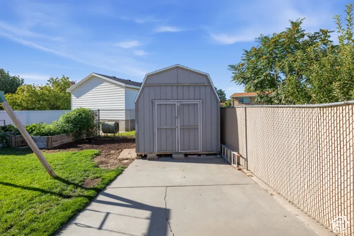 Detached storage shed with a gambrel roof and double doors, concrete pad, chain link fencing, and a raised garden bed