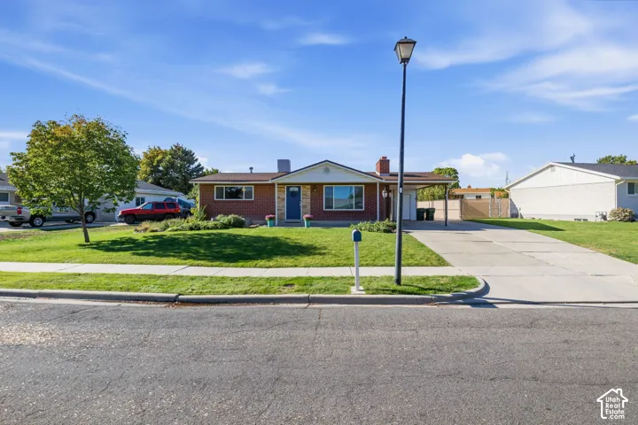 Red brick exterior with white trim, covered carport, concrete driveway, and a front lawn with established landscaping