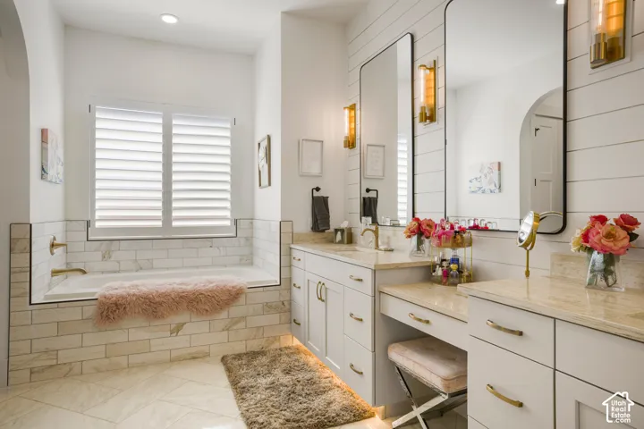 Built-in soaking tub with subway tile surround, dual vanity with undermount sinks, separate vanity area, shiplap accent wall, and tiled flooring