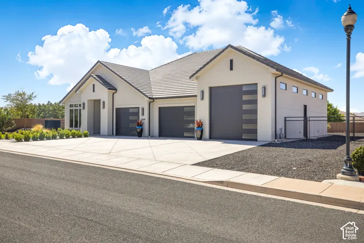 Contemporary stucco exterior with a tiled roof, multi-car garage with modern doors, and a decorative rock landscape