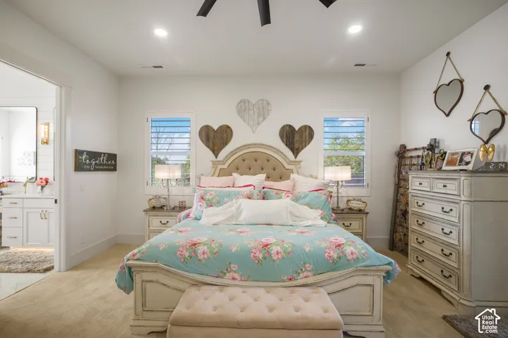 Spacious bedroom with a tufted headboard bed frame, two windows with louvered shutters, recessed lighting, and wood-finish flooring