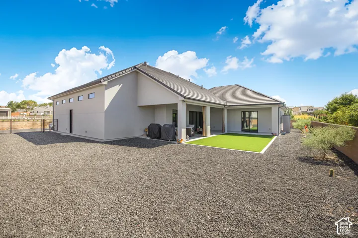 Stucco exterior with a tiled roof, featuring a covered patio, artificial turf area, and desert-style landscaping