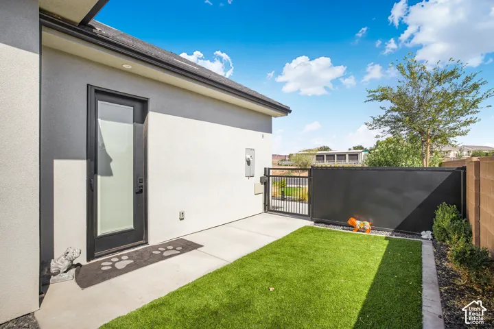Private side yard featuring artificial turf, concrete patio, and a secure metal gate with solid privacy paneling