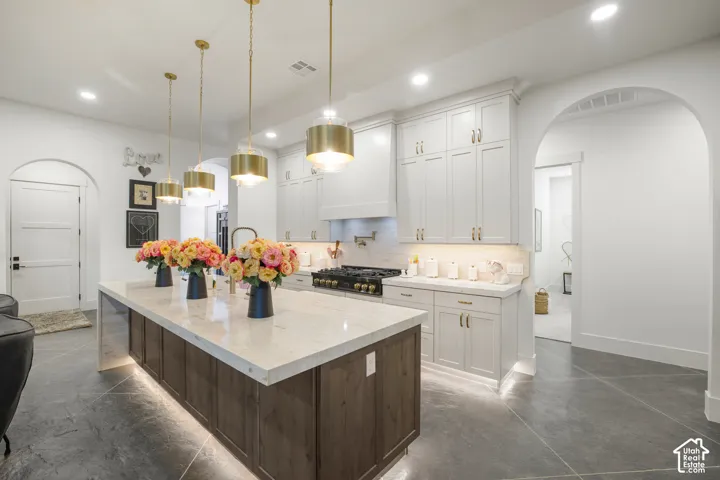 Gourmet kitchen featuring a large island with integrated lighting, a gas range, white cabinetry, and recessed lighting