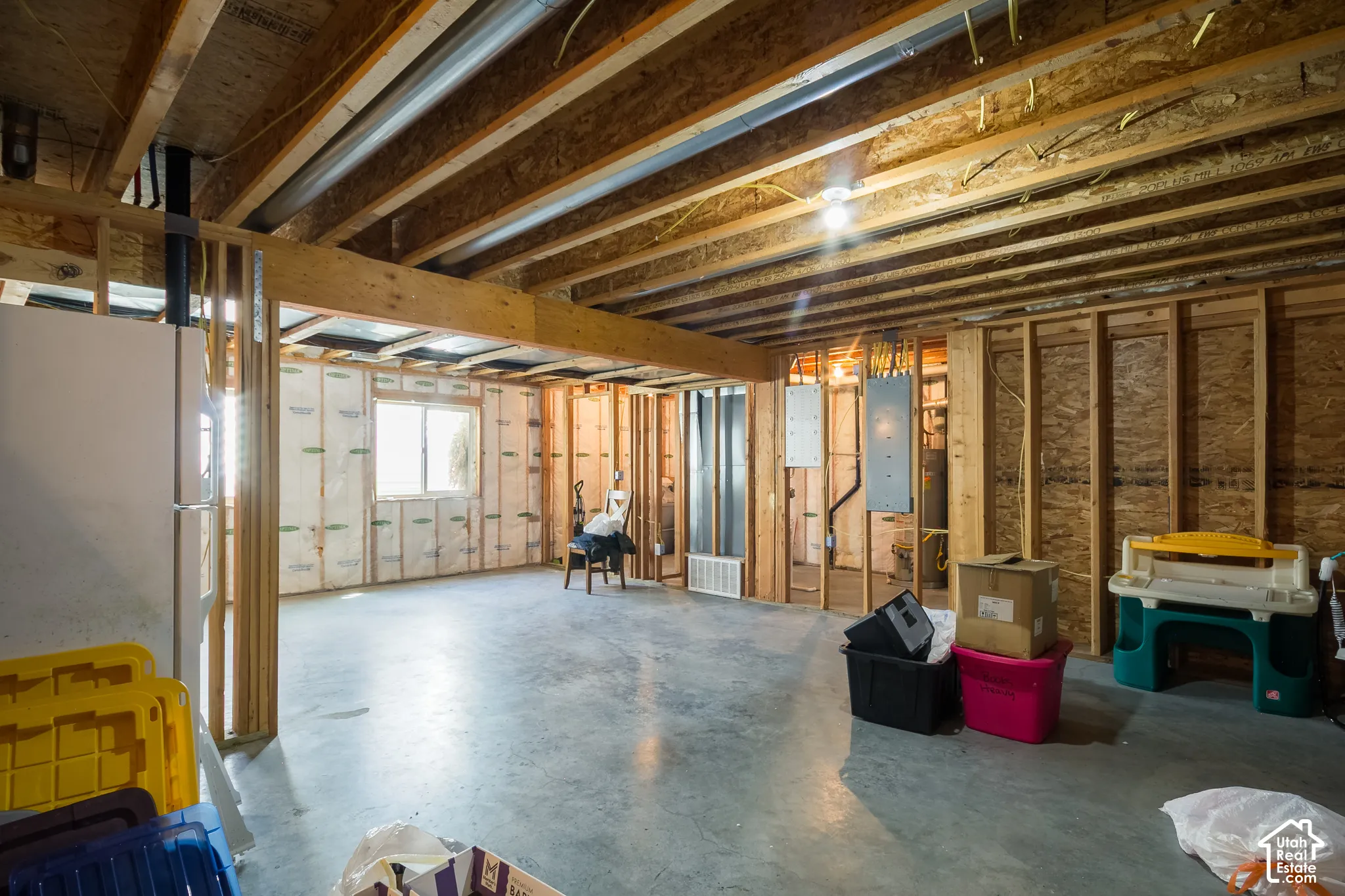 Unfinished basement with exposed wooden joists, concrete flooring, and framed walls