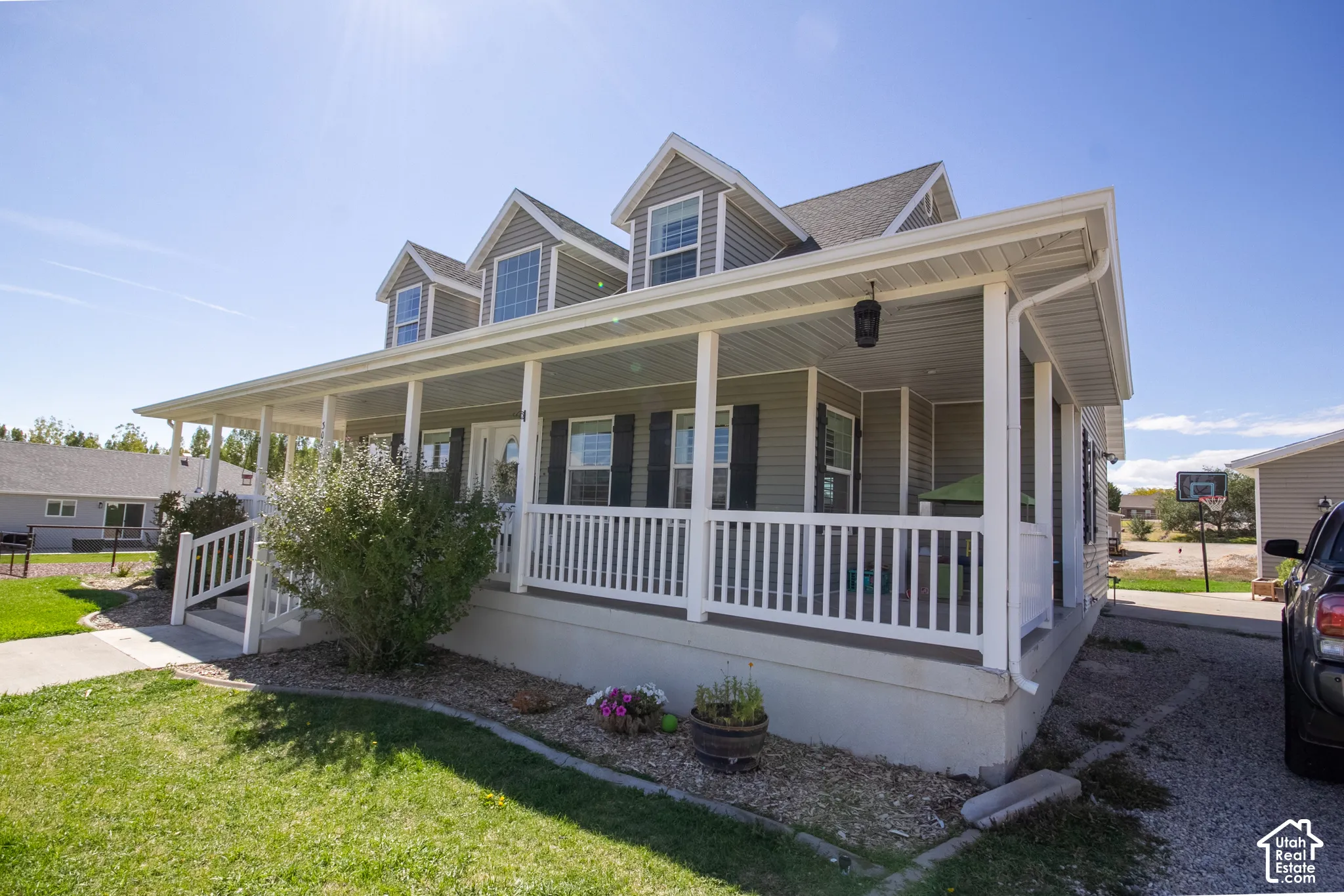 Expansive covered front porch with white railing, dormer windows, and a gravel driveway