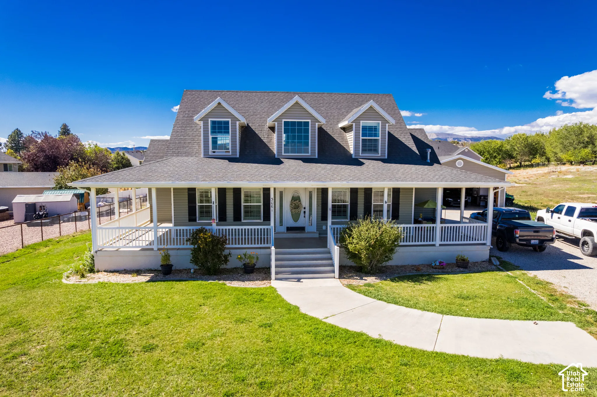 Expansive front lawn with a concrete pathway leading to a large covered front porch, featuring white railings and columns