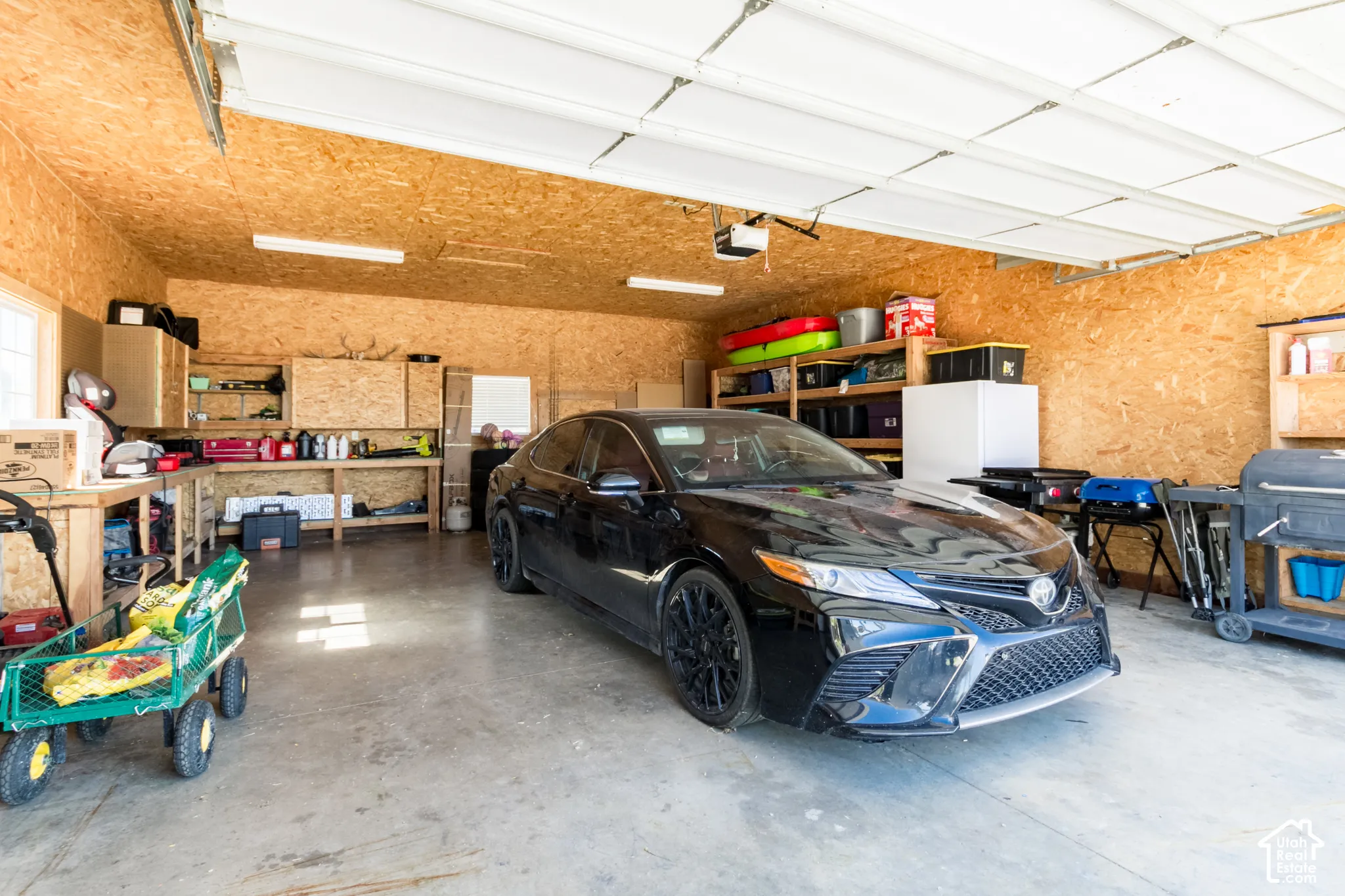 Attached garage with wood-paneled walls and ceiling, concrete flooring, and overhead lighting