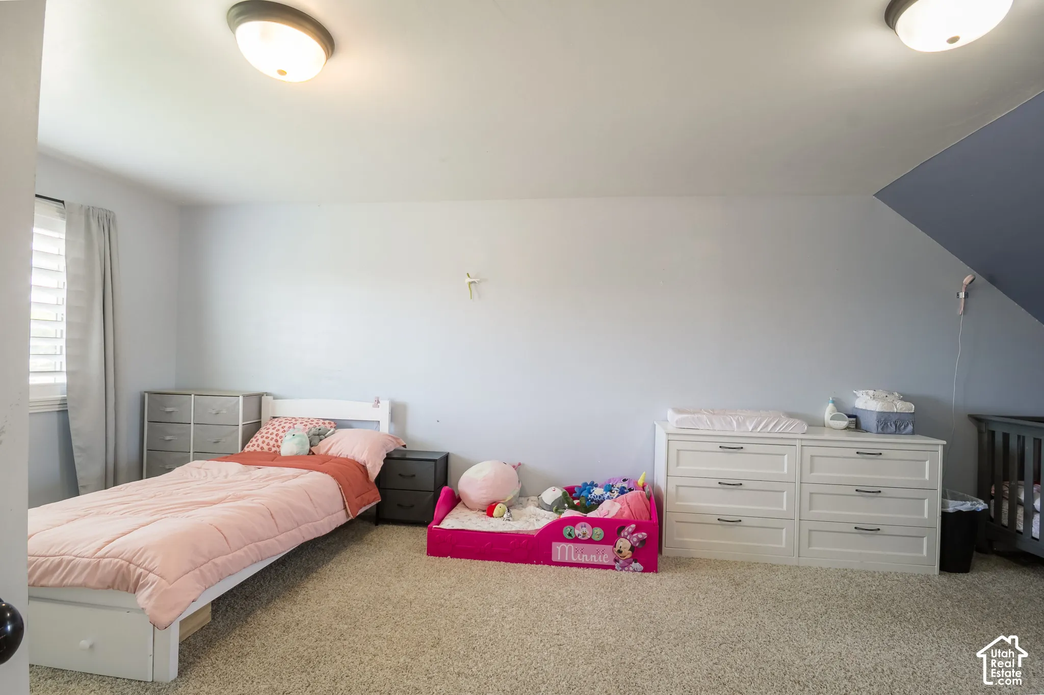 Carpeted room featuring a window with horizontal blinds, built-in ceiling lighting, and a unique sloped ceiling accent