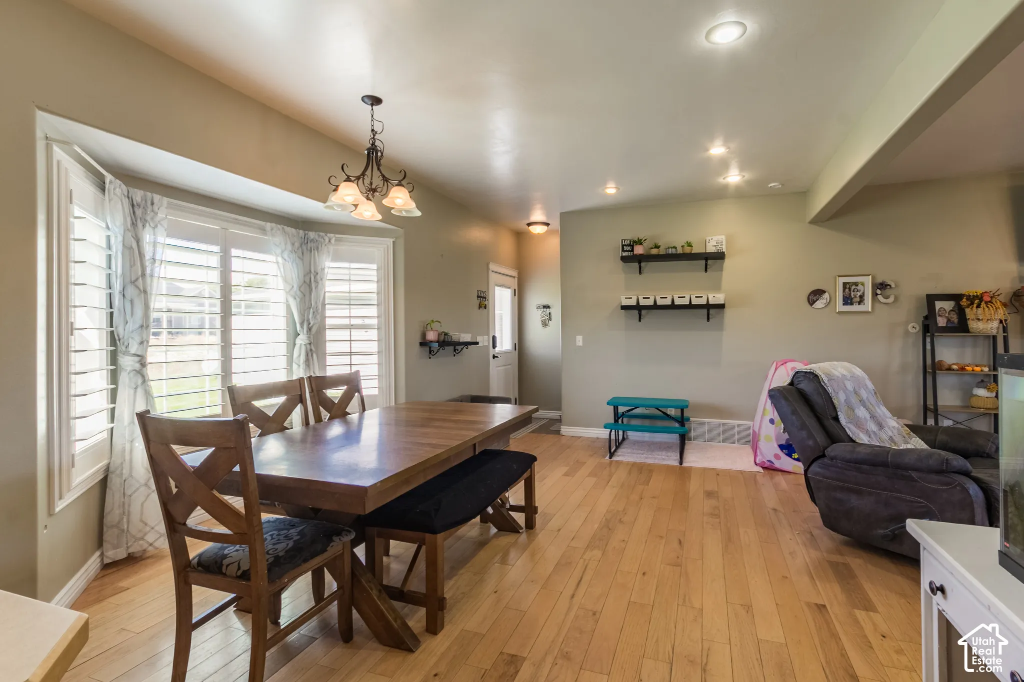 Bay window with interior shutters, wood-finish flooring, recessed lighting, and a decorative chandelier