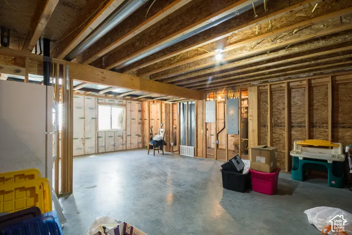 Unfinished basement with exposed wooden joists, concrete flooring, and framed walls