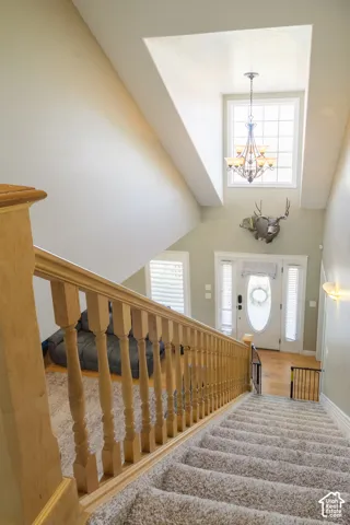 Vaulted ceiling with an upper window, chandelier, wood-finish flooring, and a staircase with wood railing