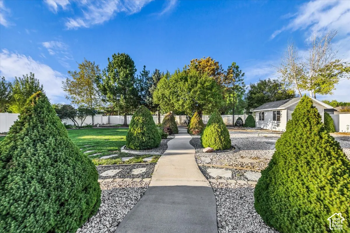 Manicured lawn, mature trees, white privacy fencing, paved pathway, and a detached storage shed w/loft & garage door