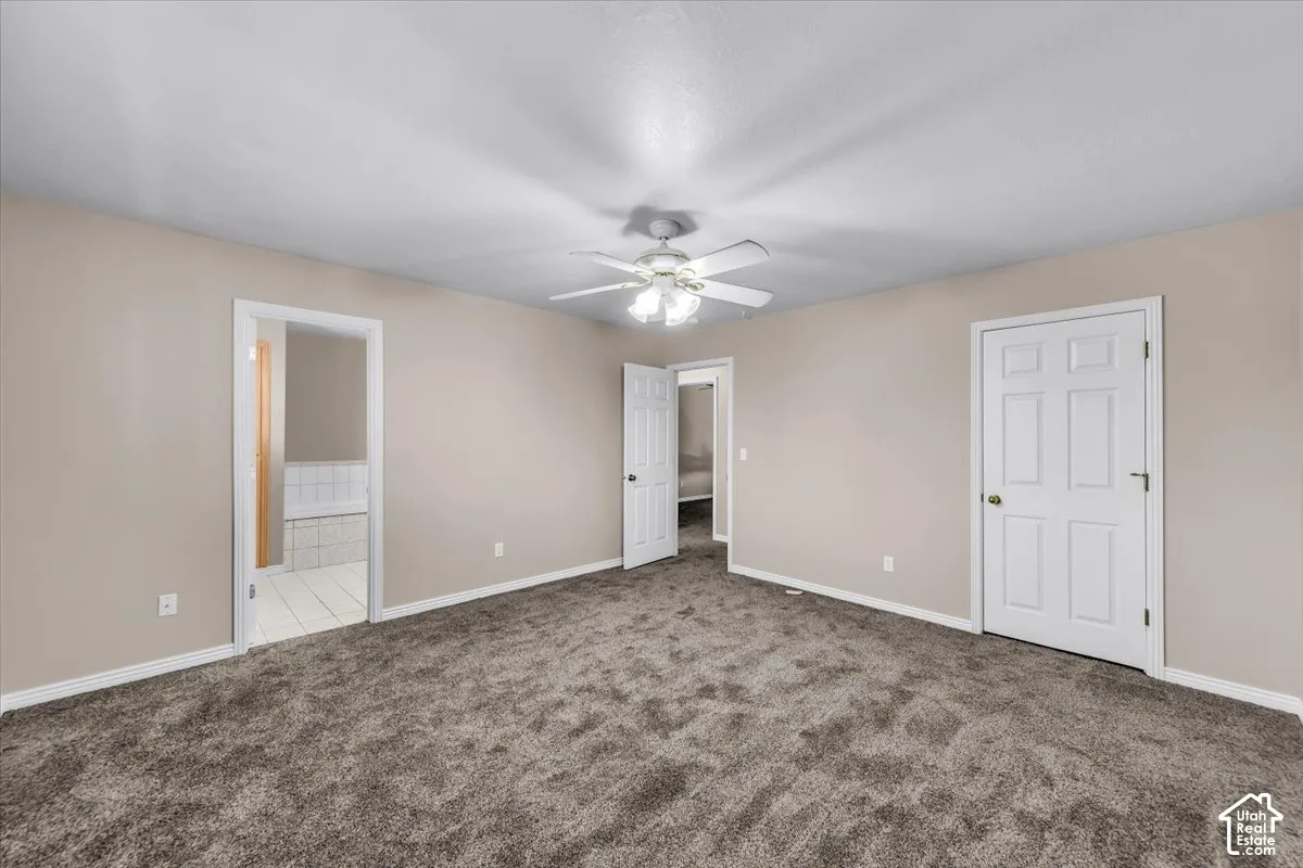 Neutral tone wall paint, textured carpet flooring, white trim, ceiling fan, and paneled doors