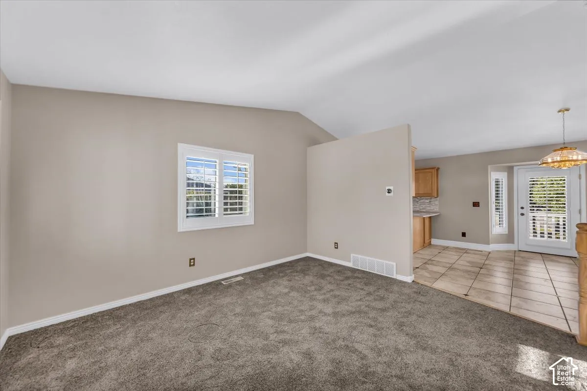 Vaulted ceiling, carpeted flooring, window with plantation shutters, tiled flooring, wood cabinetry